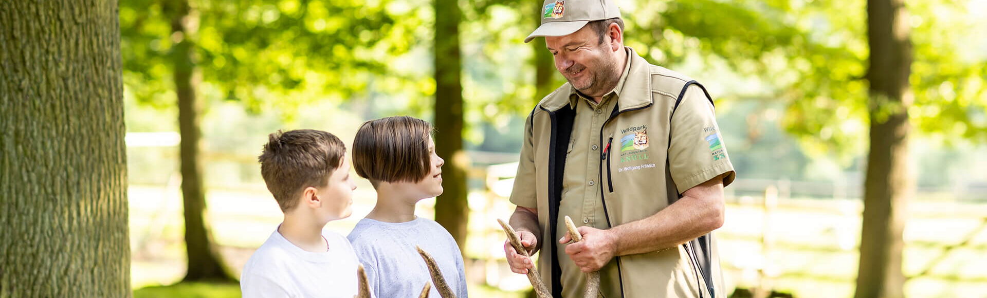 Wildparkleiter Dr. Fröhlich erklärt zwei Jungs das Geweih eines Hirsches.